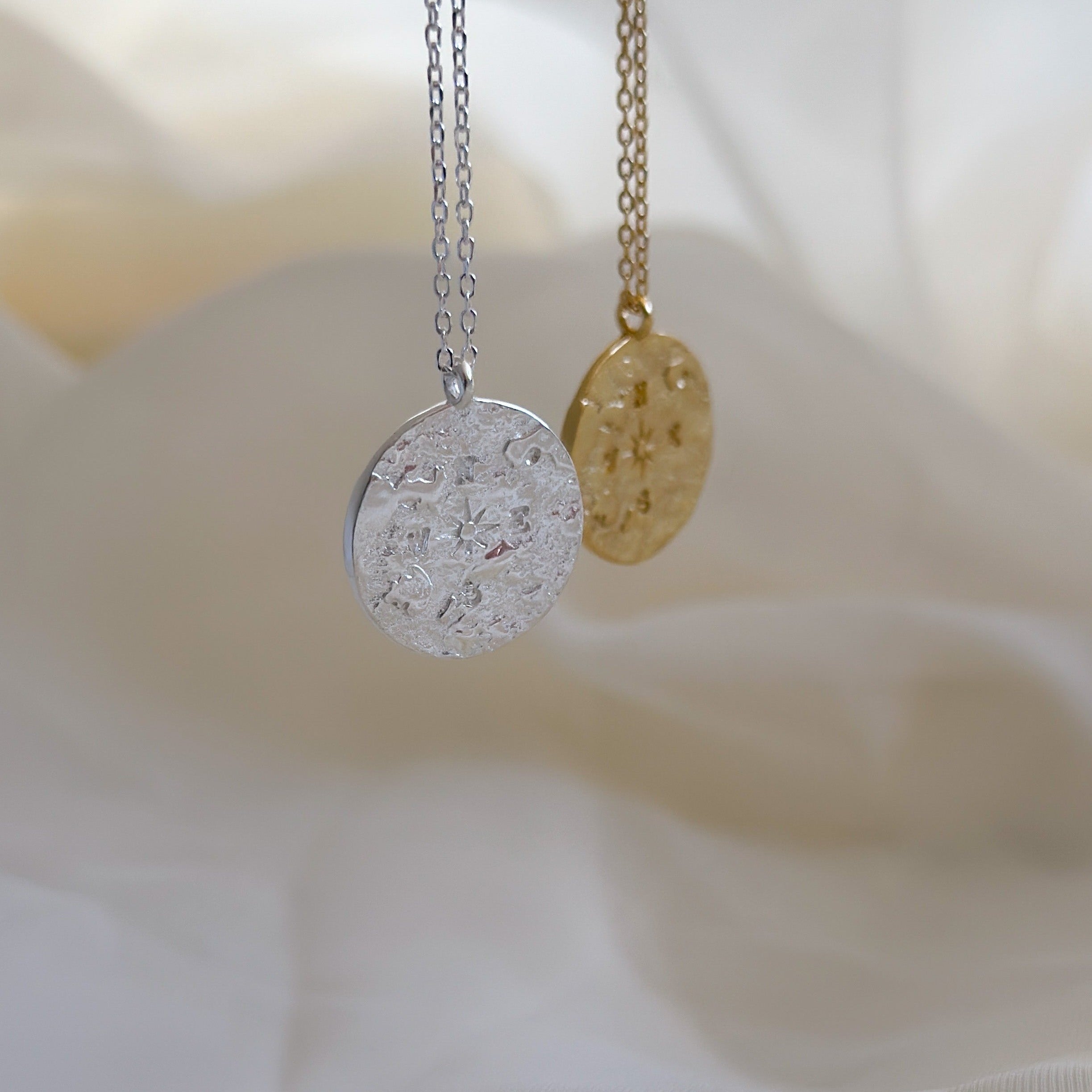 Zwei Anhänger-Ketten in Silber und Gold auf hellem Stoff