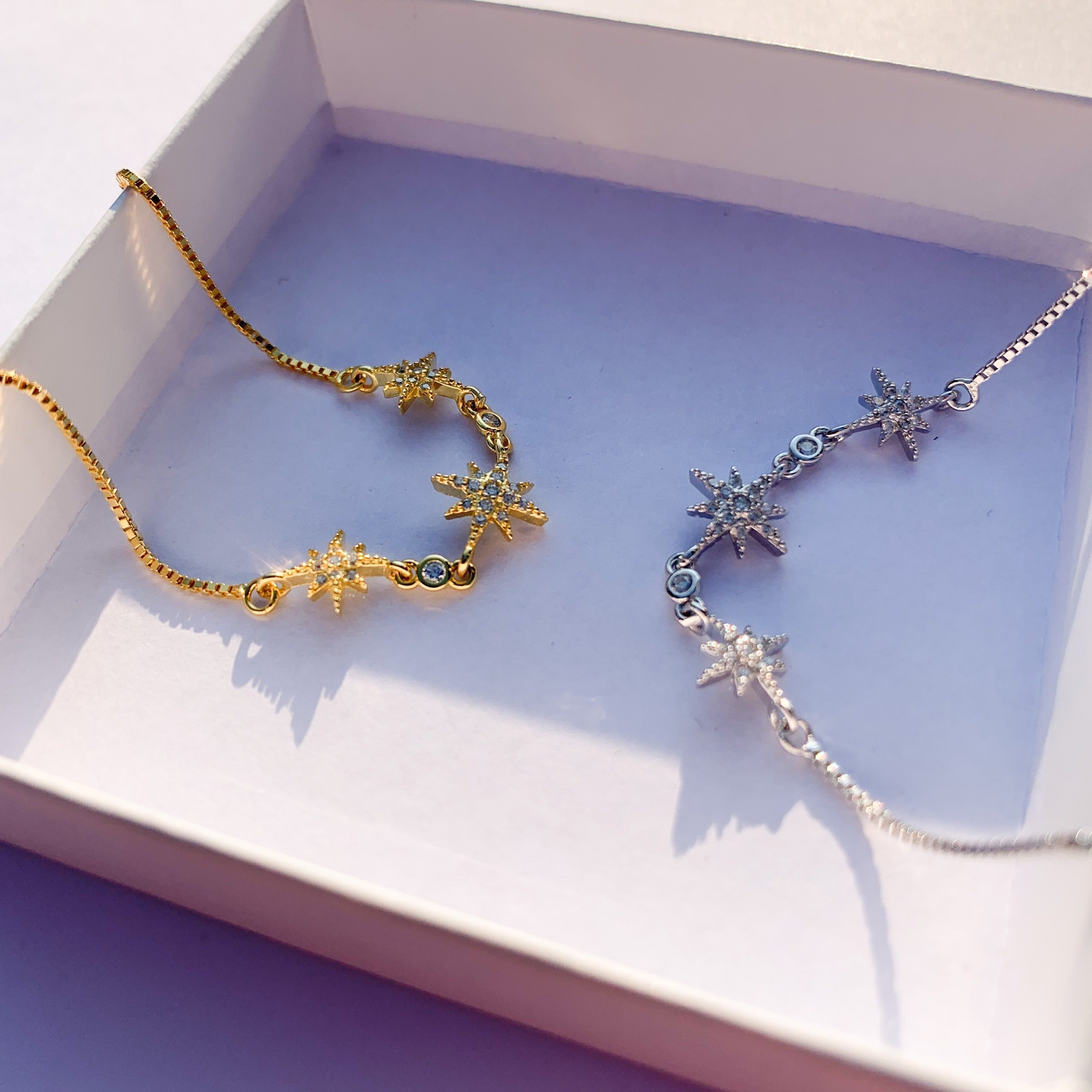 Zwei Stern-Armbänder in Gold und Silber in einer weißen Geschenkbox