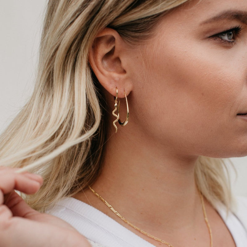 A model wears the Golden Clara ear hoops, layered with the Serenity snake hoops in her 2nd piercing. Clara is oval in shape and hangs low at 2cm